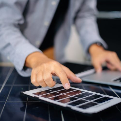 Engineer using tablet near solar panel and wind turbine model, representing clean energy, green innovation, and smart technology in modern engineering.